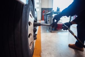Mechanic working in a professional automotive service shop tightening bolts on a large vehicle wheel using a power tool. The image illustrates automotive repair concepts, technical skills, and workshop activities.